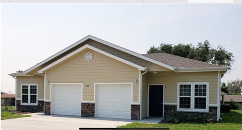 a tan house with two garage doors and a driveway