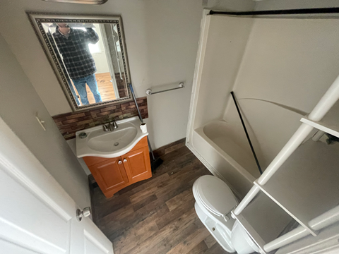 A man is taking a picture of a bathroom with a sink, toilet, and mirror.