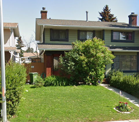 A green lawn in front of a house with a flower bed in the front.