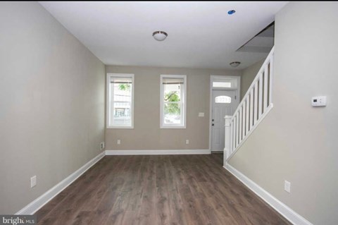 A spacious room with wooden floors and a staircase on the right side.