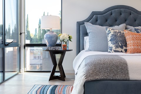 A bedroom with a bed, a table with a vase and a lamp.