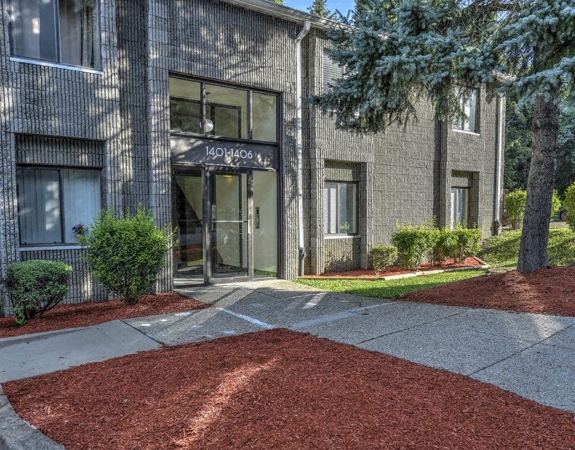 front entrance of an apartment building with a gravel driveway and trees