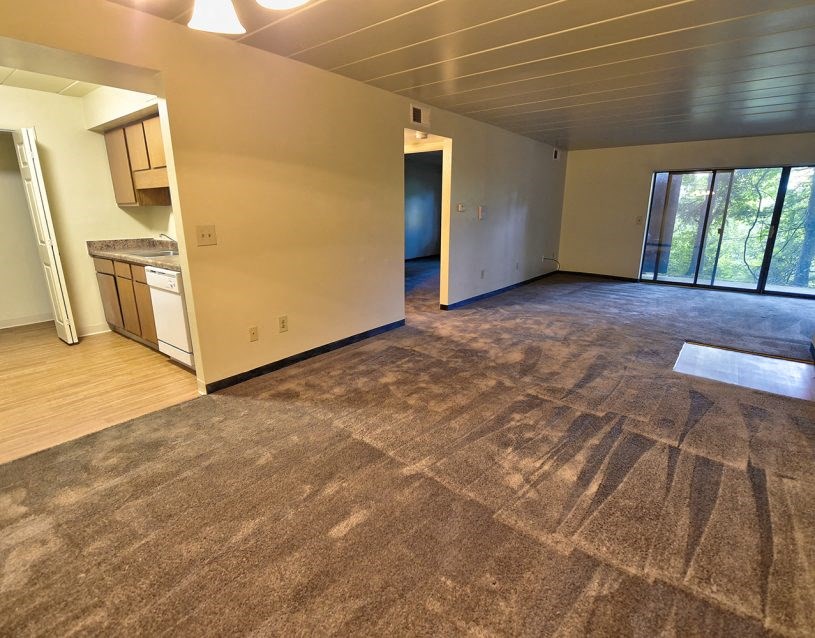 an empty living room with a kitchen and a window