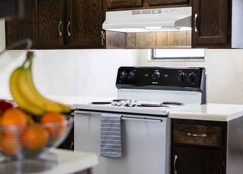 A kitchen with a stove and a bowl of fruit on the counter.