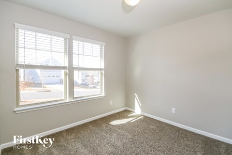 A room with a carpet floor, a window with blinds, and a view of a street outside.