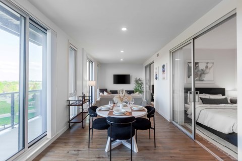 A modern dining room with a table set for two and a bedroom in the background.
