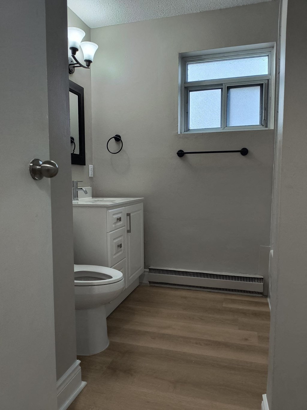 A bathroom with a toilet, sink, and a window.
