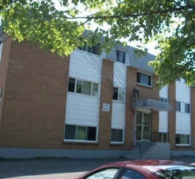 A red car is parked in front of a building with a white and brown facade.
