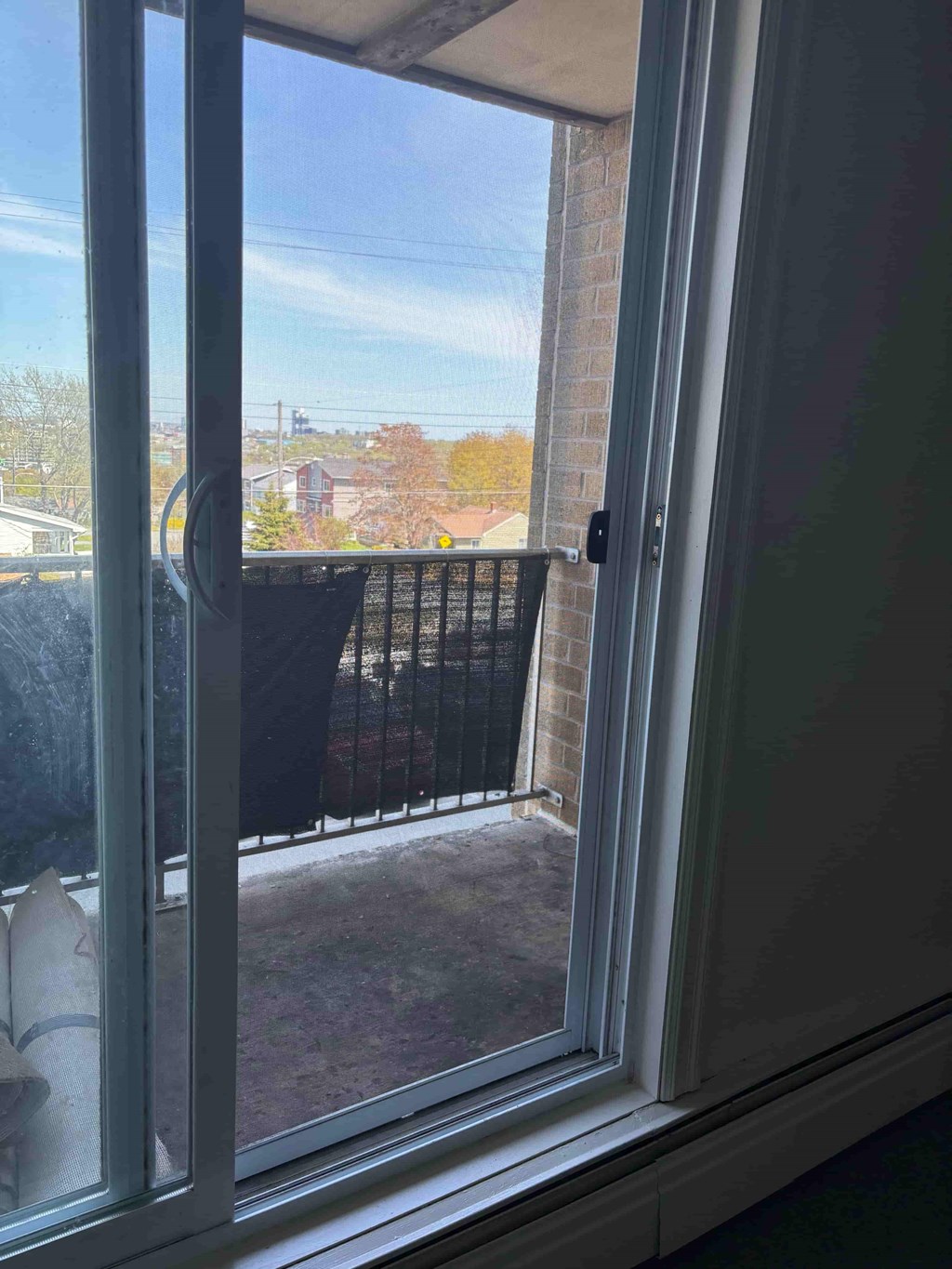 A view from inside a room looking out through a window to a balcony with a black railing.