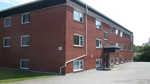 A red brick building with a black awning and a parking lot in front.