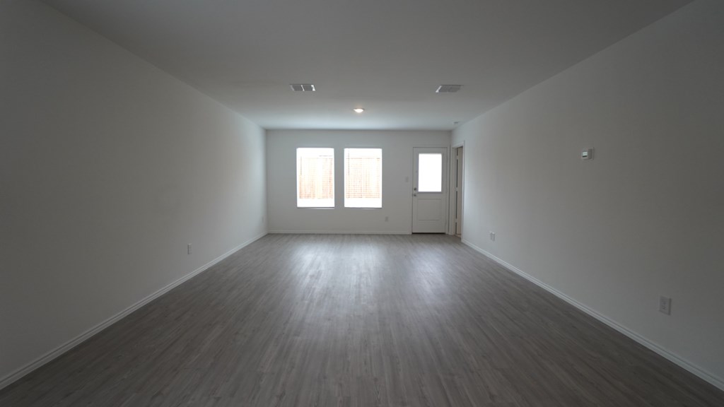 A large empty room with wooden floors and two windows.