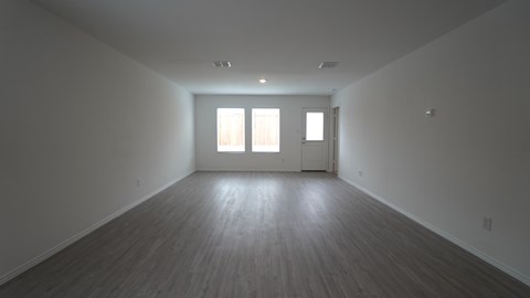A large empty room with wooden floors and two windows.