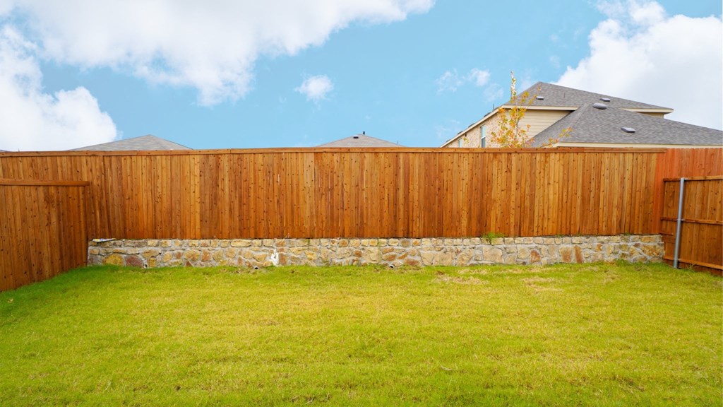 A wooden fence with a stone pillar separates a grassy area from a house.
