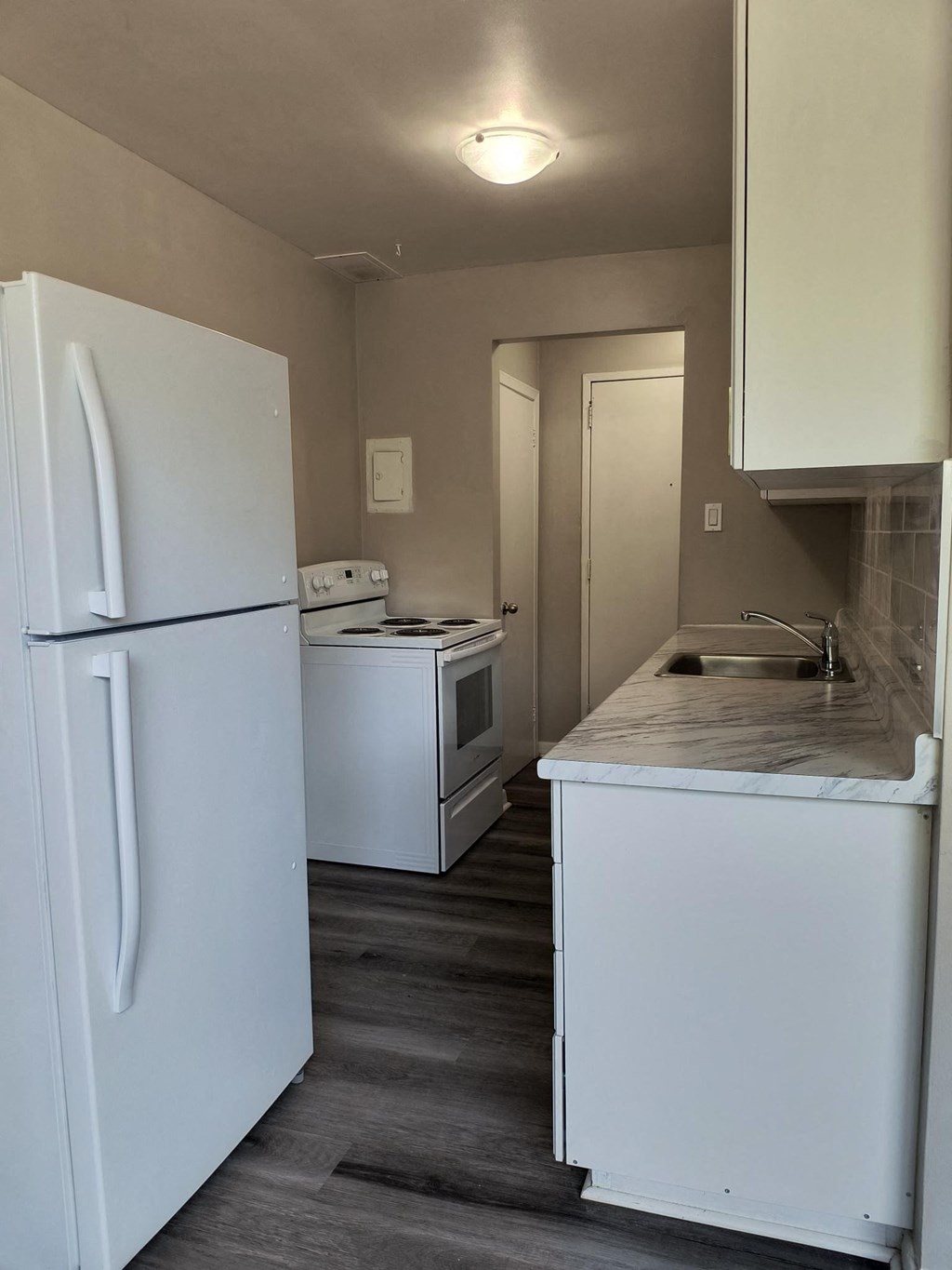 A small kitchen with a white fridge and a white sink.