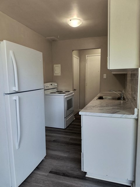 A small kitchen with a white fridge and a white sink.