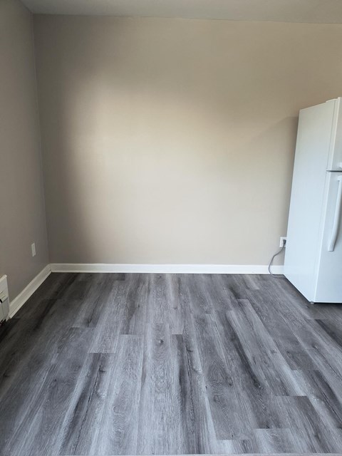 A room with a white fridge and wooden flooring.
