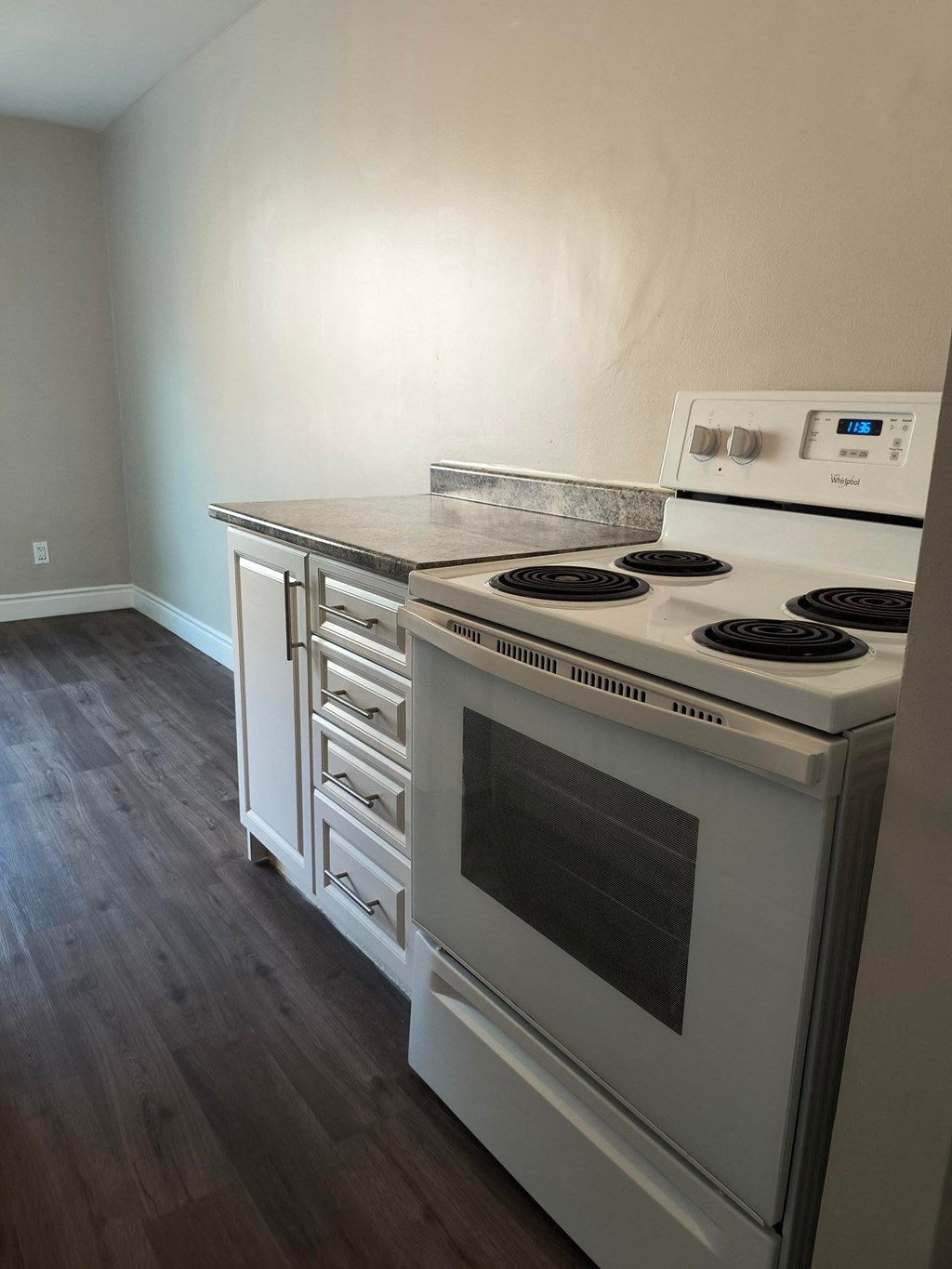 A white stove with a digital display is in a room with wood flooring.