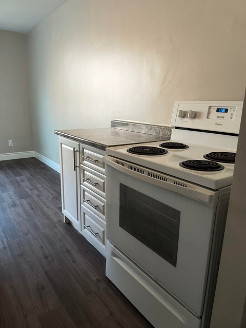 A white stove with a digital display is in a room with wood flooring.