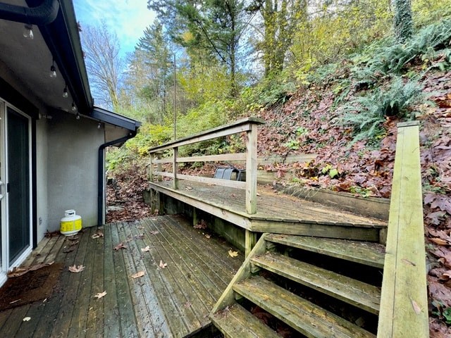 a deck with stairs next to a house in the woods