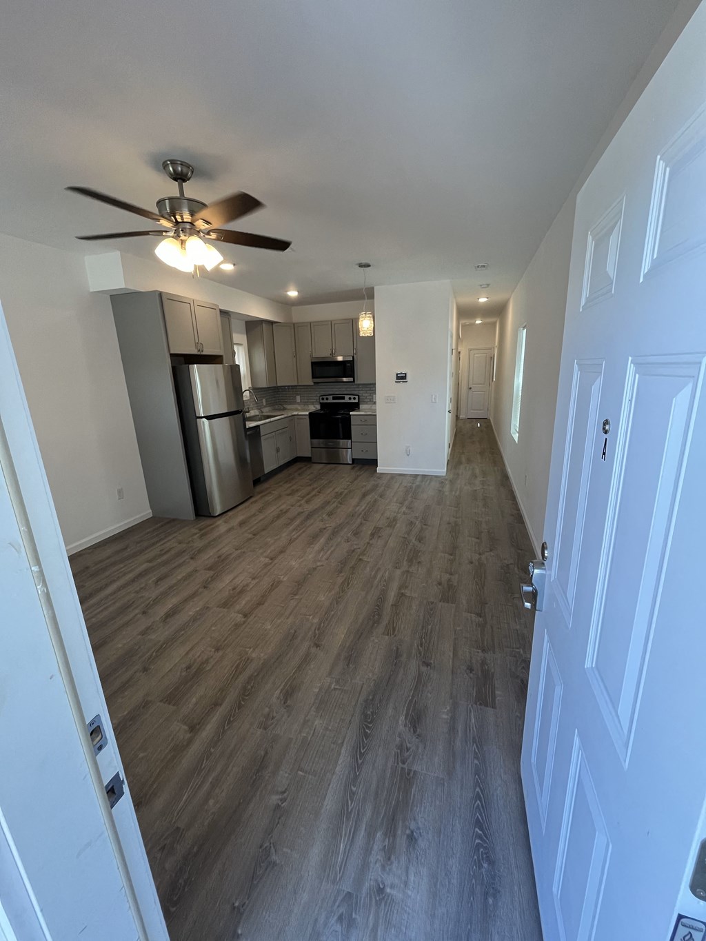 an empty living room and kitchen with wood floors and a ceiling fan