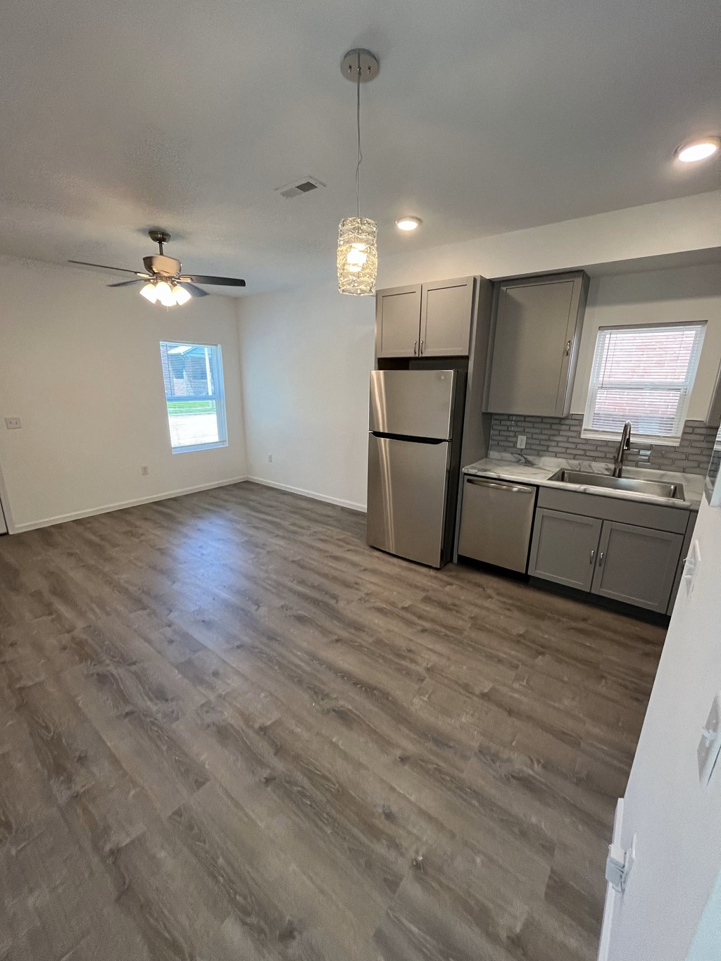 an empty living room with a kitchen and a ceiling fan