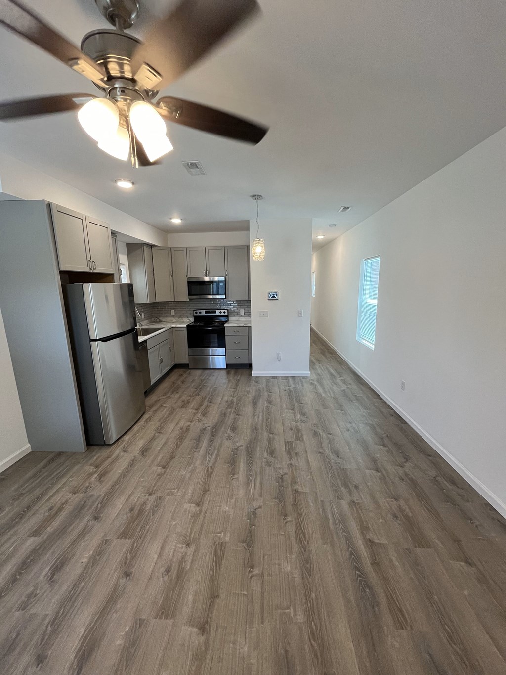 an empty living room and kitchen with wood flooring and a ceiling fan