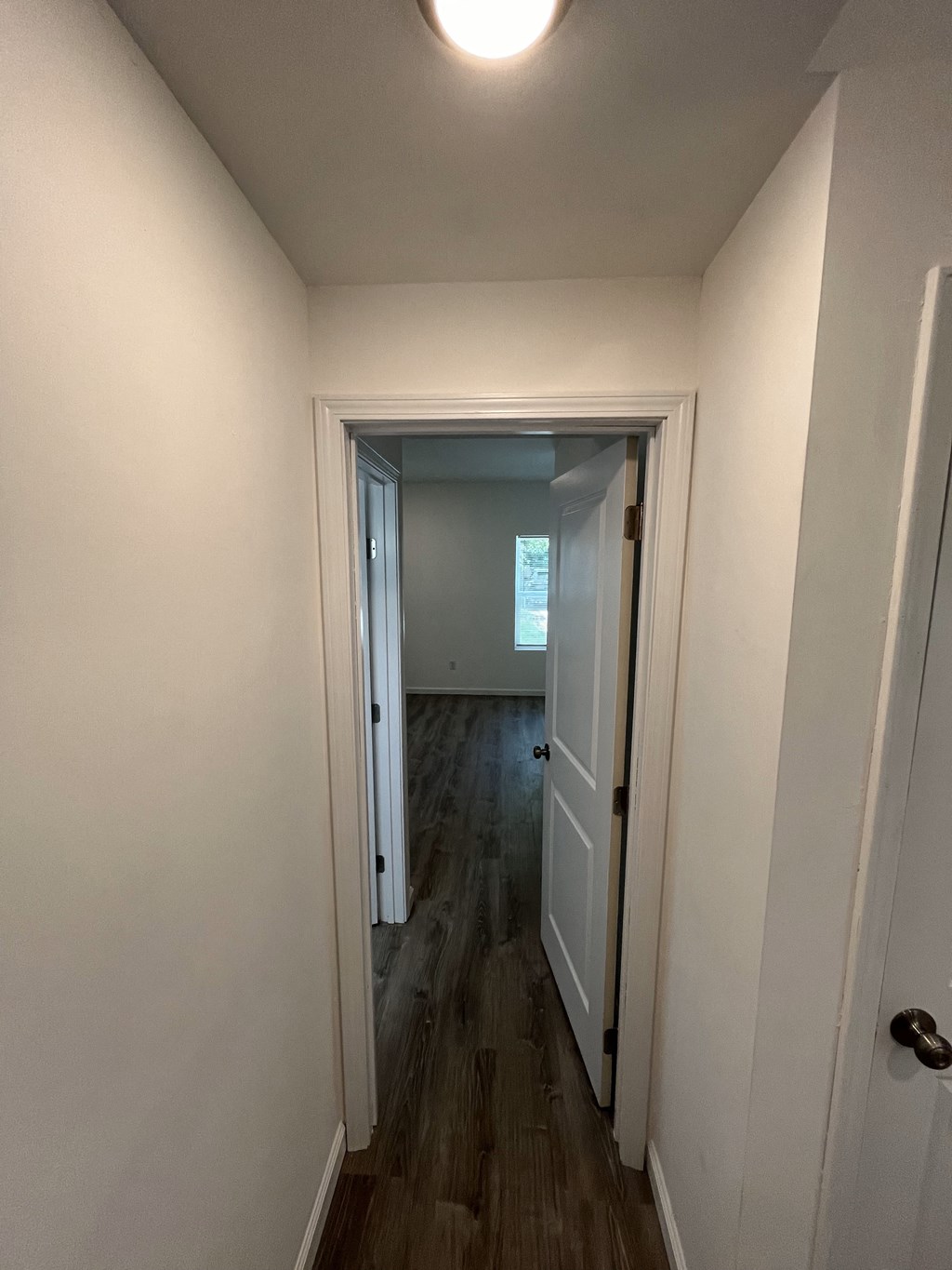 a small hallway with a door open to a room with white walls and wood floors