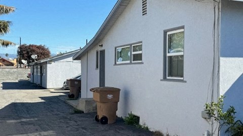 A white house with a brown trash can in front of it.