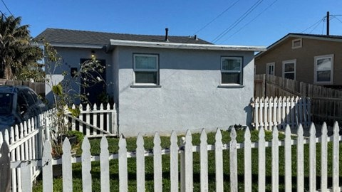 A white picket fence in front of a grey house.