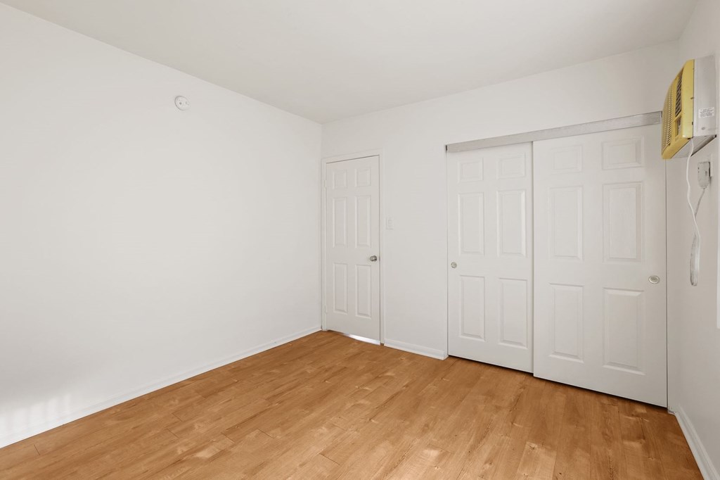 A room with white walls and wooden flooring with two white doors.