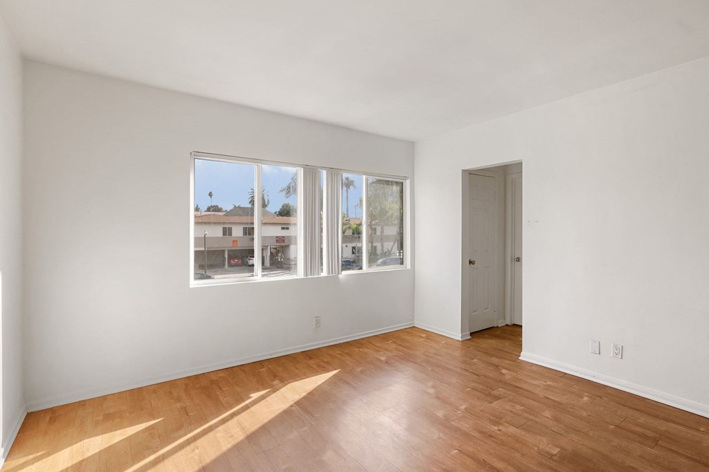 A room with white walls and wooden flooring with a view of a building outside the window.