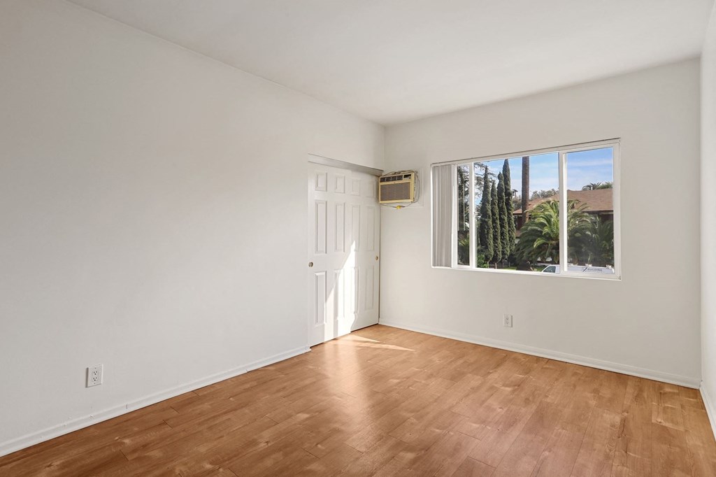 A room with wooden flooring and a window showing an outdoor view.