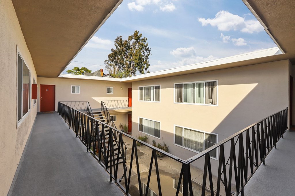 A balcony with a black railing and a building with a red door.