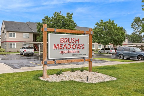 A sign for Brush Meadows Apartments stands in a grassy area.