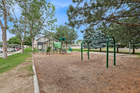 A playground with a green swing set and a red dirt ground.
