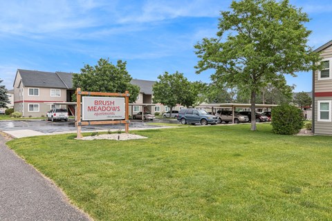 A sign for Brush Meadows Apartments stands in front of a grassy area.