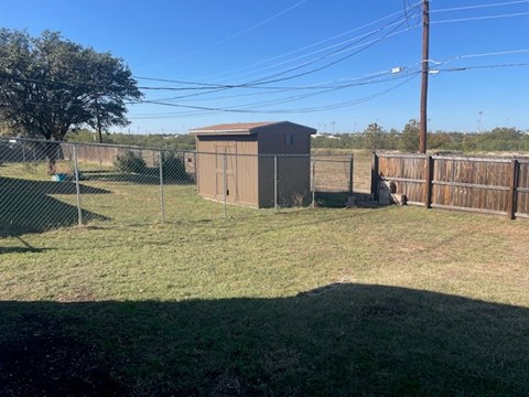 A small brown shed sits in a grassy field next to a fence.