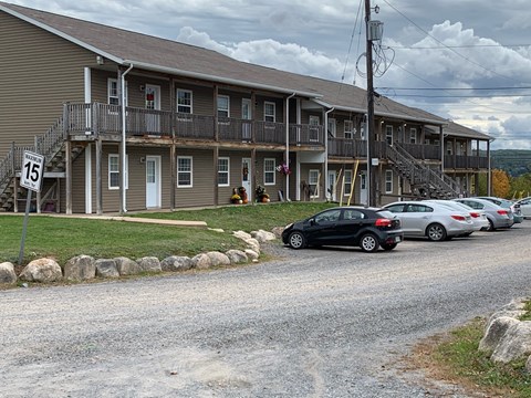 A black car is parked in front of a two-story apartment building.