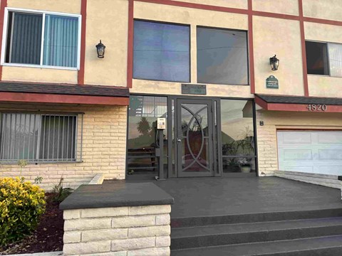 A building with a red and beige facade has a black gate and steps leading to the entrance.