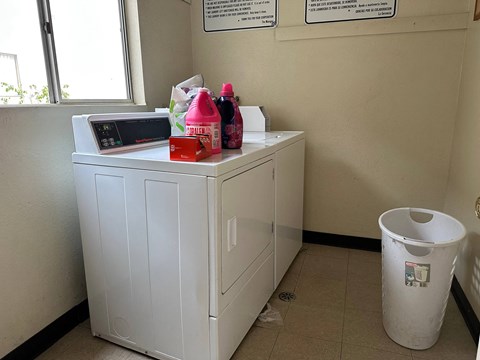 A white washing machine sits in a room with a trash can and a window.