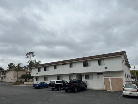 A parking lot with a white building and cars parked in front.