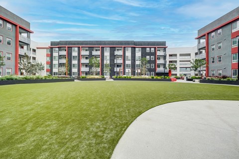 A grassy area in front of a building with red and grey balconies.