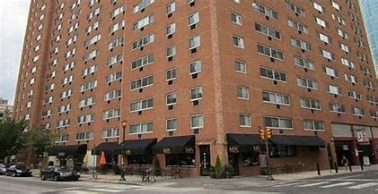 A tall brick building with many windows and a street in front.