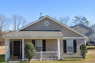 A small house with a porch and a tree in front.