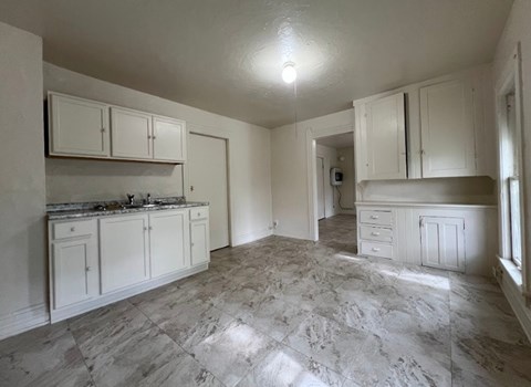A kitchen with white cabinets and marble flooring.