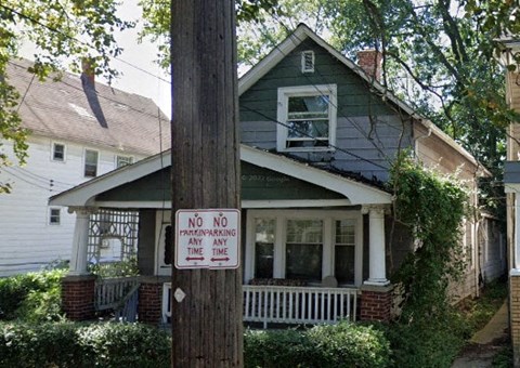 A sign on a pole in front of a house states "NO PARKING ANY TIME".