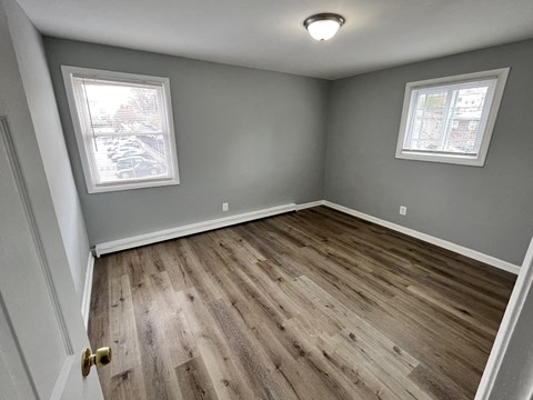 A room with wooden flooring and two windows.