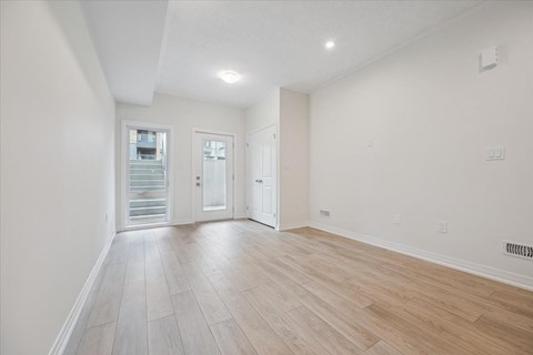 A spacious room with light wood flooring and white walls.
