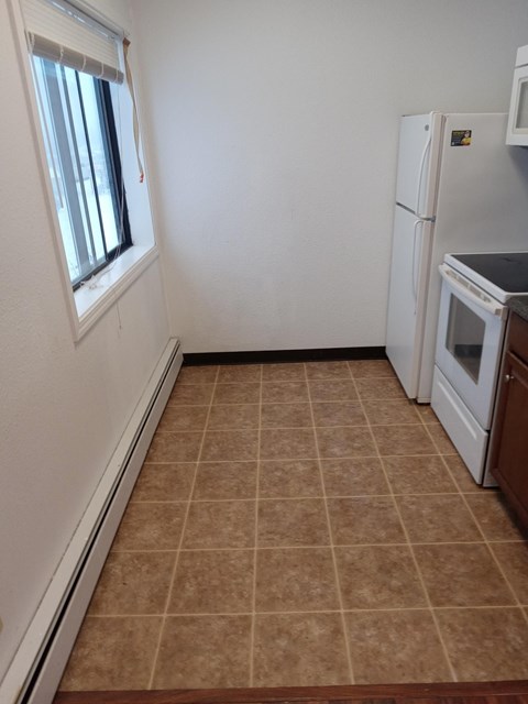 A kitchen with a white refrigerator and brown tiled floor.