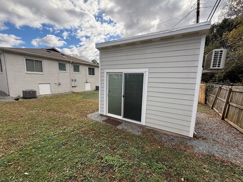 A small white shed with a green door is situated in a grassy area.